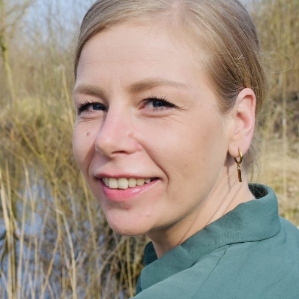 Porträt einer Frau mit blonden Haaren vor natürlichem Hintergrund, lächelnd