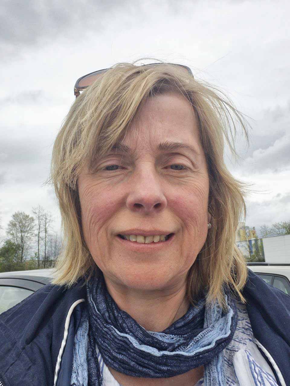 Frau mit blonden Haaren, Sonnenbrille auf Kopf, Porträt mit Parkplatz im Hintergrund