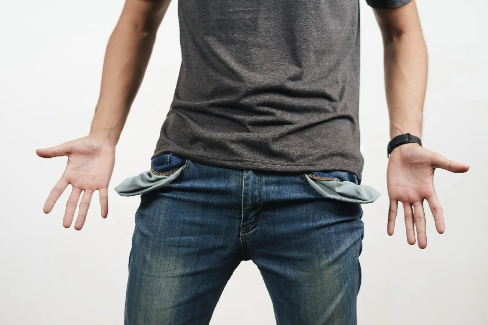 TikTok Marketing Insider-Hacks – Videokurs für Affiliate-Umsatz 6 Mann in grauem T-Shirt und Jeans mit leeren Hosentaschen, Arme ausgebreitet vor weißem Hintergrund