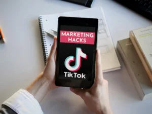 Tablet in Händen zeigt TikTok Marketing Hacks Startbildschirm auf Schreibtisch mit Notizbuch und Büchern