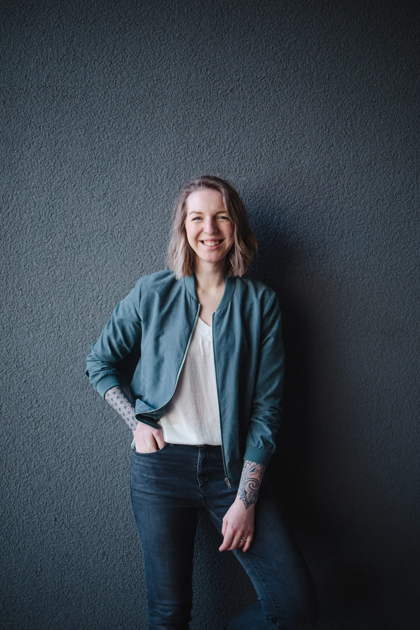 Porträt von Luisa Häußer, Markenstrategin, in Jeans und Blazer vor grauer Texturwand