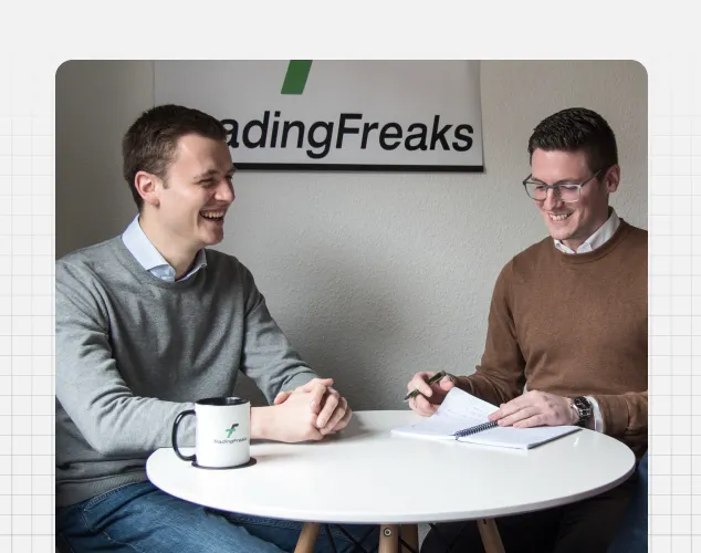 Zwei männliche Trading-Freaks-Mitarbeiter im Gespräch am Tisch mit Kaffeetasse