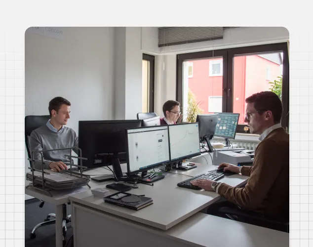 Arbeitssituation mit drei männlichen Mitarbeitern im Büro am Schreibtisch mit Monitoren