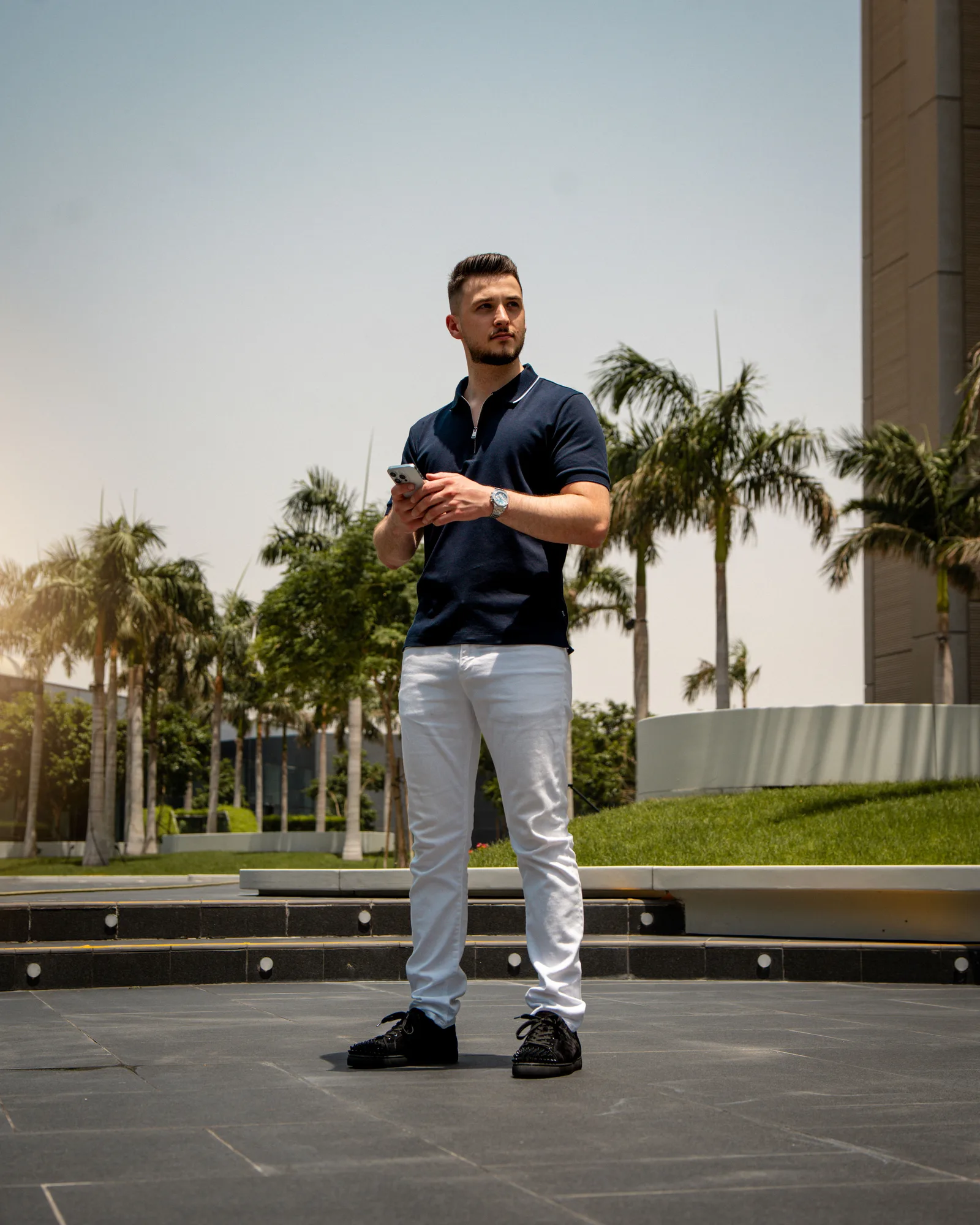 Thomas Wimmer steht auf einer Terrasse mit Smartphone in der Hand, trägt dunkles Poloshirt und weiße Hose
