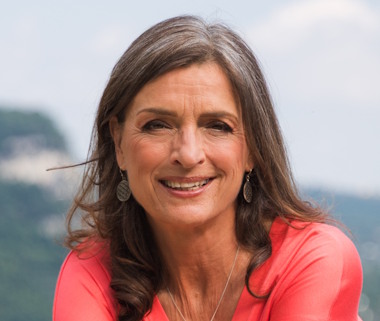 Hermine Theresia Thrä lächelnd vor Berglandschaft, rotes Oberteil