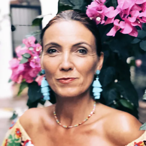 Frau mittleren Alters vor pinken Blüten, Halskette und Ohrringe, ruhiger Blick