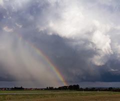 Sommergewitter mit Regenbogen über Landschaft und dunklen Wolken