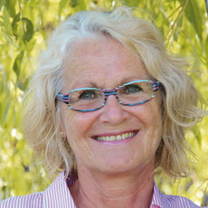 Portrait von Astrid Jackstein, Frau mit weißem Haar und Brille vor gelblichem Hintergrund
