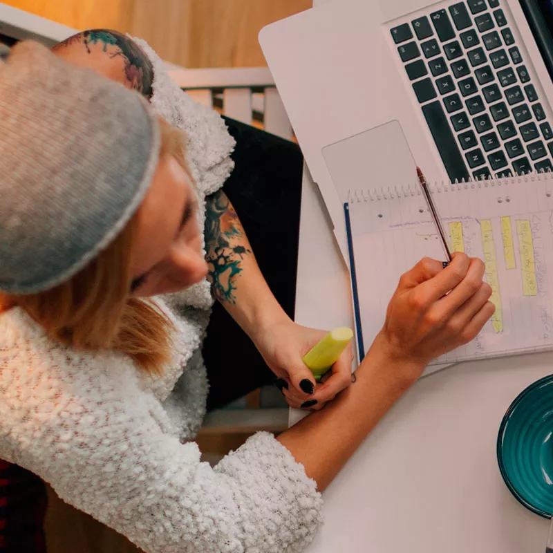 Frau von oben beim Arbeiten am Laptop, Notizen und Apfel auf Tisch