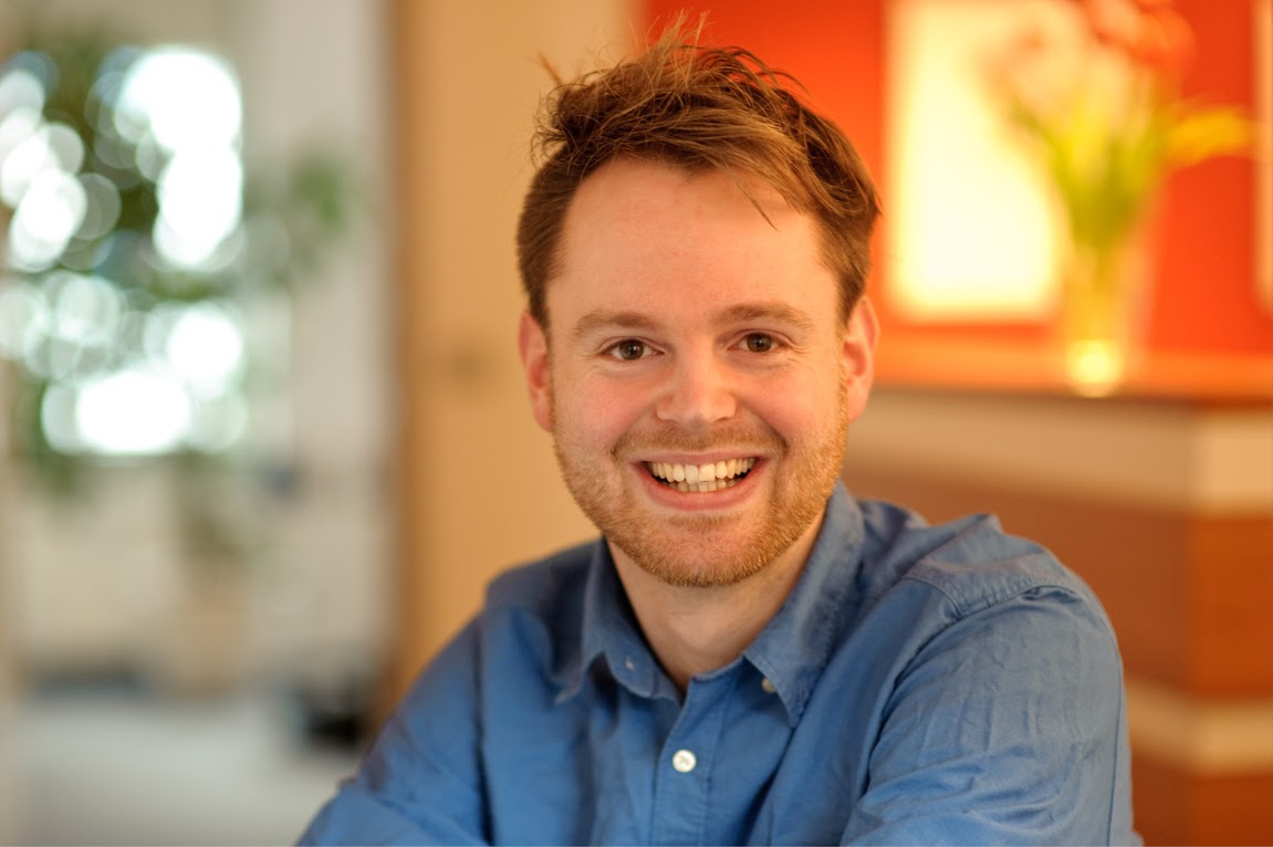 Christoph Marks, Autor des VED-Online-Seminars, lächelt in die Kamera vor orangem Hintergrund