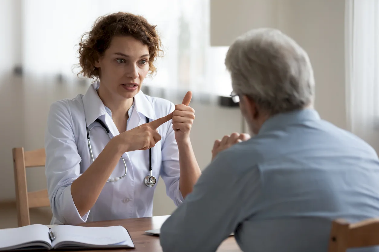 Junge Ärztin gestikuliert beim Erklären während Gesprächszweisamkeit mit älterem Patienten