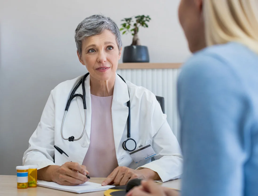 Ärztin im weißen Arztkittel führt nachdenkliches Gespräch mit Patientin im Behandlungszimmer
