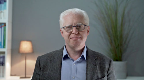 Portrait des Kurs-Dozenten mit Brille im Business-Hemd vor neutralem Hintergrund
