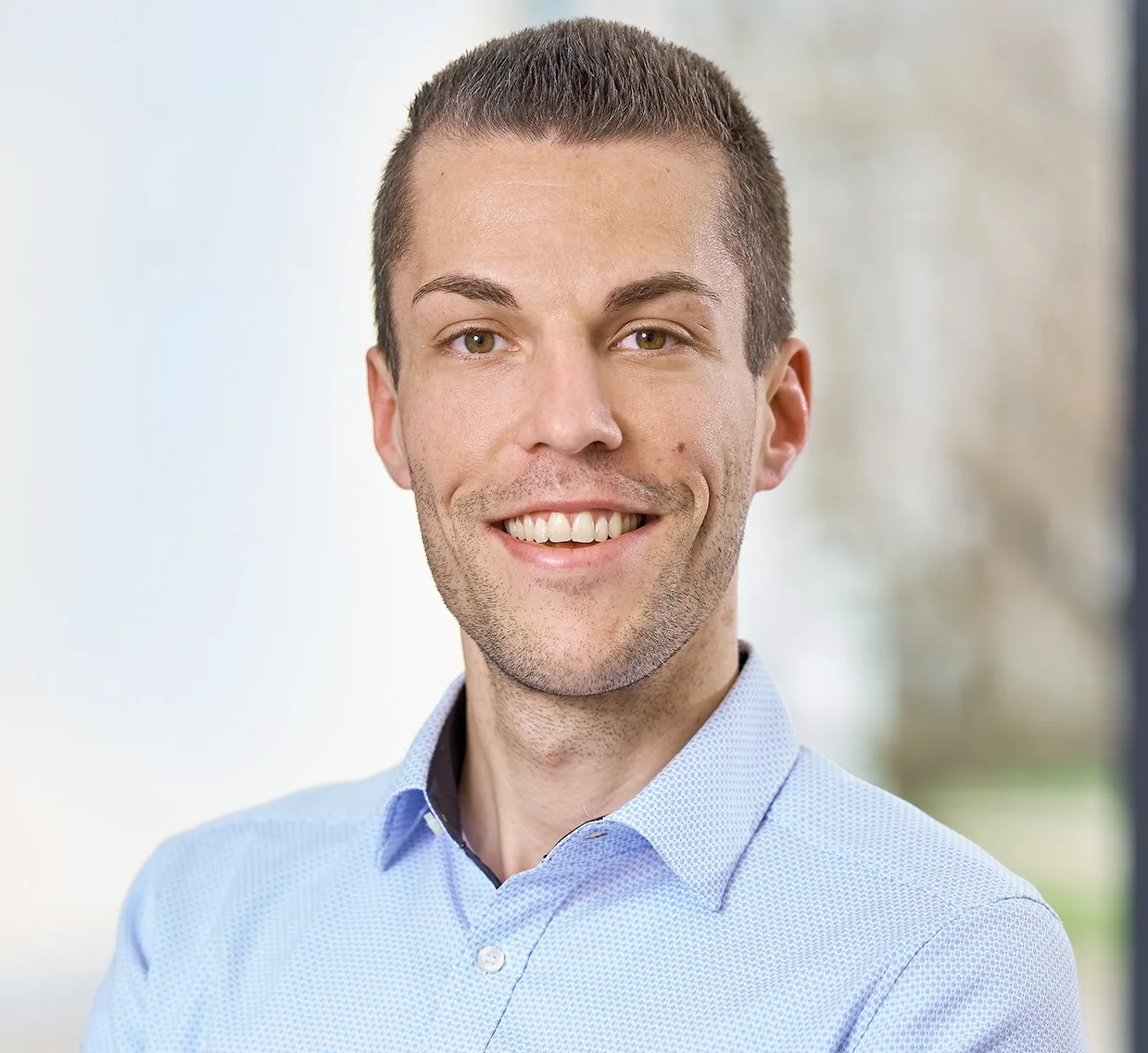 Porträt eines lächelnden Mannes in hellem Poloshirt mit unscharfem Hintergrund