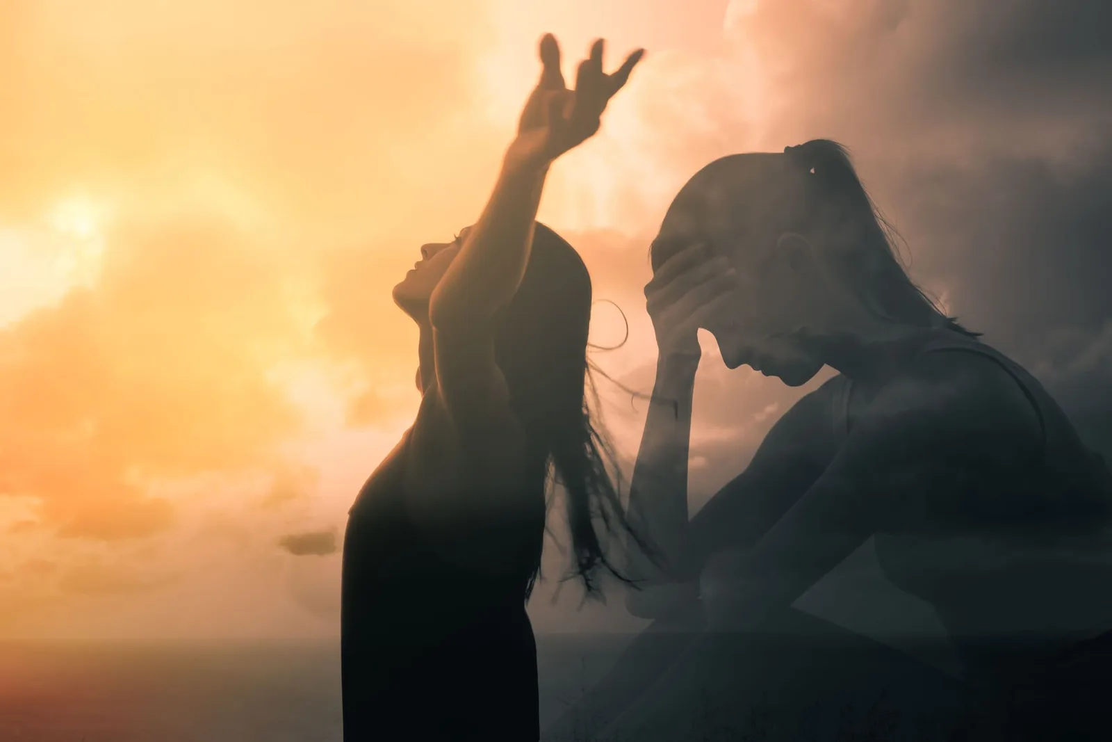 Zwei Frauen im Gegenlicht bei Sonnenuntergang mit erhobenen Armen in emotionaler Pose