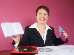 Frau im Business-Outfit vor rosa Hintergrund mit Feng-Shui-Kompass und Grundrissen