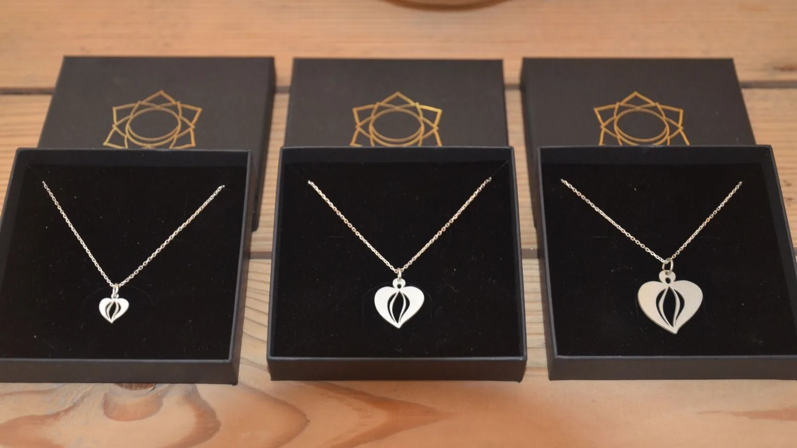 Visionskarten Atelier – Videokurs zur Zielklarheit von Sina Seybold 8 Drei schwarze Schmuckboxen mit goldener Sonnen-Mandala aufgeklappt, zeigen Yoniheart-Anhänger in Silber an Ketten