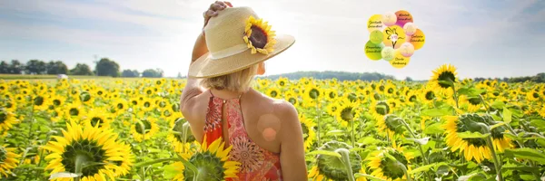 Frau mit Strohhut in Sonnenblumenfeld mit Produktflaschen im Hintergrund