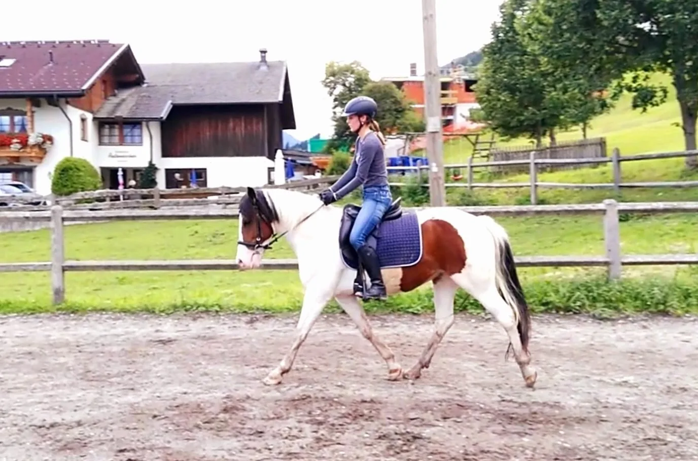 Reiterin auf zweifarbigem Pferd beim Training auf Reitplatz mit Gebäuden