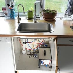 Autarke Osmoseanlage unter Spüle mit schwarzem Waschbecken und grünen Pflanzen
