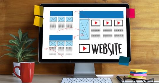 Monitor zeigt Website-Layouts und Wireframes mit Navigationsmenü und Inhaltsbereich neben Tastatur