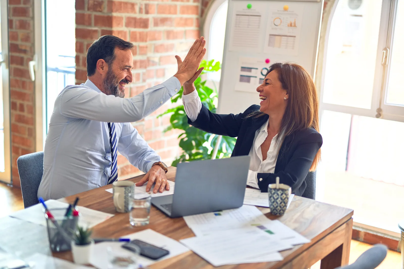 Webinar-Bundle – Videokurse zur Bewerbung von Tanja Herrmann-Hurtzig 8 Zwei Berufstätige geben sich High-Five im Büro mit Laptop und Dokumenten