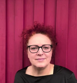 Barbara Valenti mit hochgesteckten roten Locken vor pinkem Vorhang, freundlicher Blick