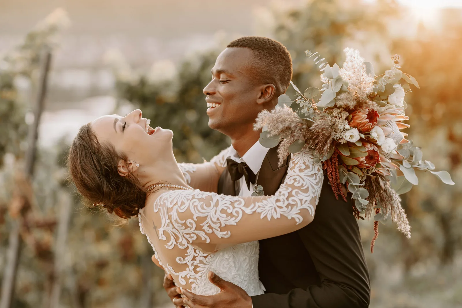 Brautpaar beim Hochzeitstanz, Bräutigam trägt die Braut, romantische Gartenkulisse mit Blumenstrauß