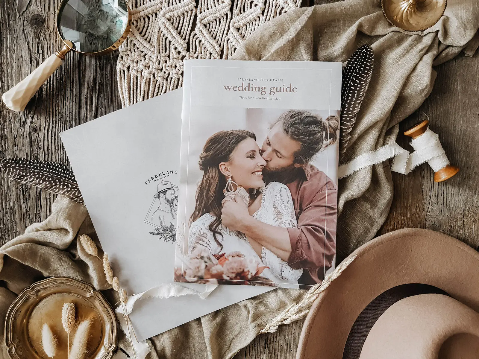 Wedding Guide auf Holztisch mit Blumen, Tüchern und Dekoelementen in Erdtönen, Flat-Lay