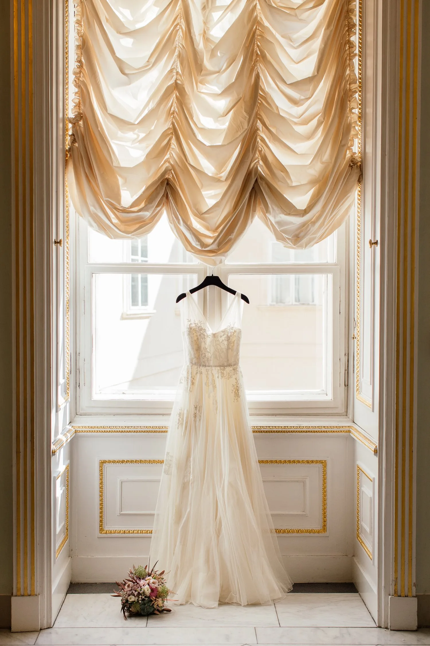 Brautkleid an Bügel im Albertina Wien vor Fenster mit goldenen Vorhängen und Brautstrauß