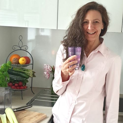 Nicoletta Poddey mit Saftglas in der Küche, Gemüse und Obst im Hintergrund