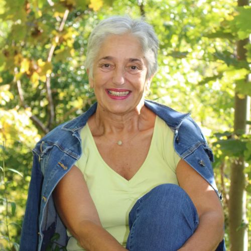 Uschi Eichinger lächelnd im Grünen, Porträtfoto mit weißem Shirt und Jeansjacke