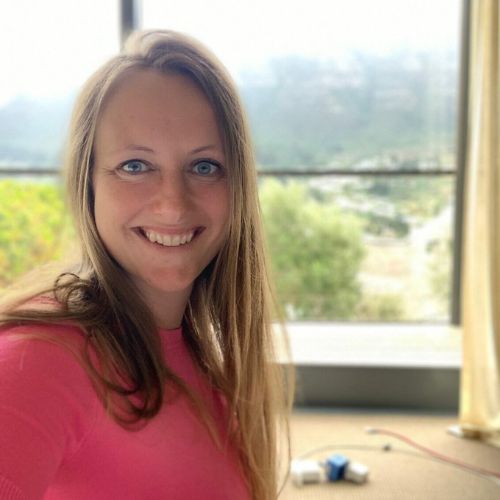 Porträt von Anja Hecht, Frau mit langen braunen Haaren im rosa Top vor Fenster mit grüner Landschaft