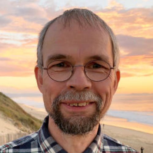 Porträt von Dr. Michael Scholze, Mann mit Brille und Bart vor Sonnenuntergang am Strand