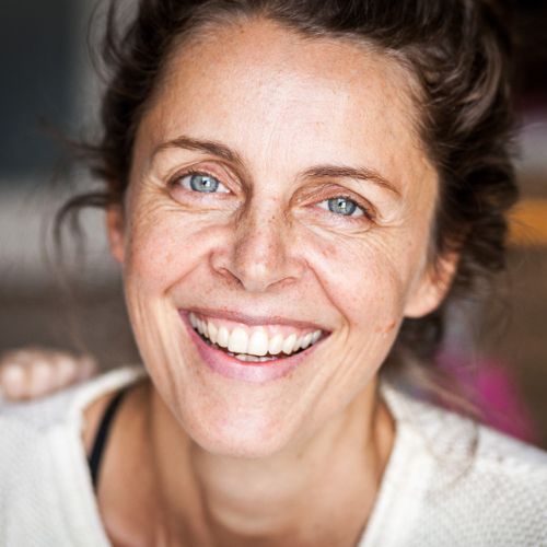Porträt von Erika West, Frau mit braunen Haaren und breitem Lächeln vor unscharfem rosa Hintergrund