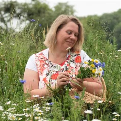 Blonde Frau mit Wildkräutern in den Händen vor grünem Wald