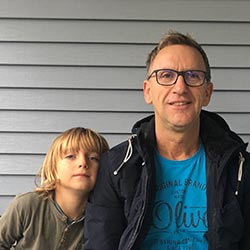 Portrait Micha Peter mit Kind vor grauer Holzwand