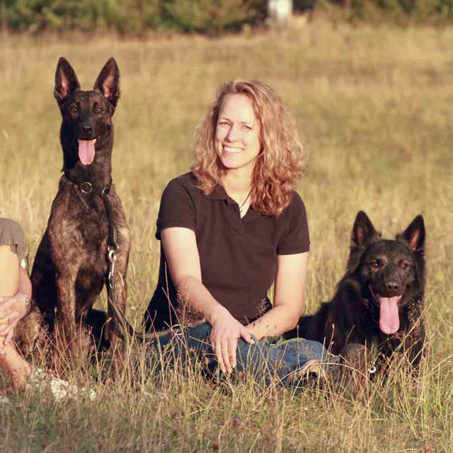 Nadine Thuß mit zwei schwarzen Deutschen Schäferhunden auf Wiese sitzend