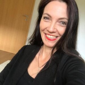 Profilbild: Lächelnde Frau mit schwarzen Haaren, roten Lippen, schwarzem Blazer