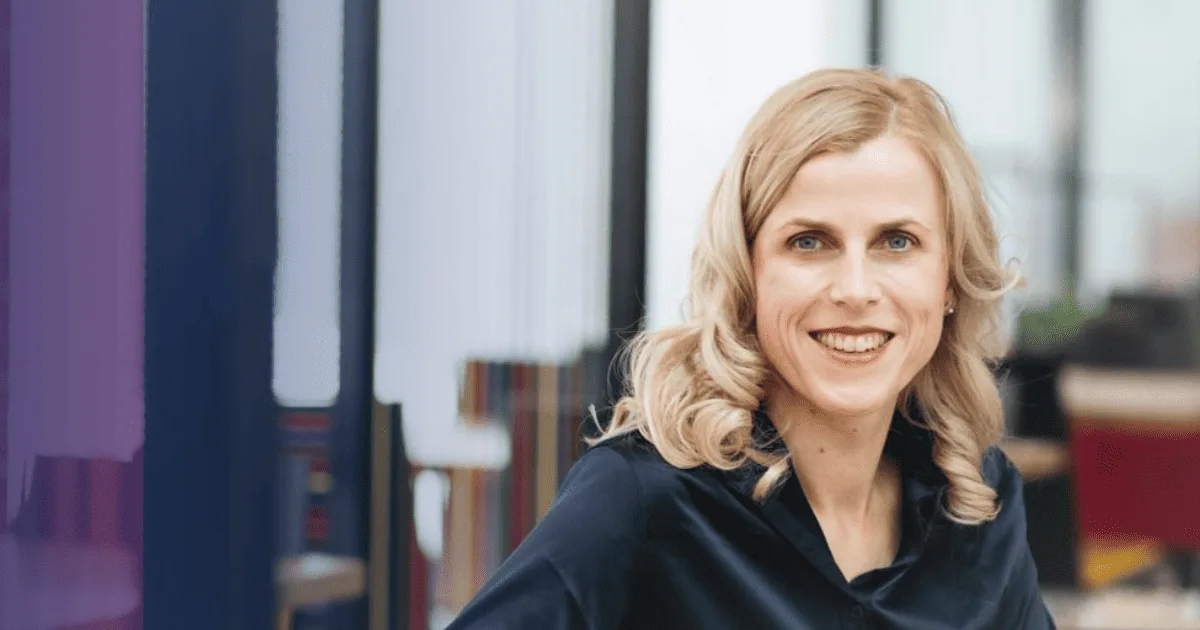 Dr. Andrea Maria Bokler, blonde Frau in schwarzer Bluse, lächelnd vor modernem Büro-Hintergrund