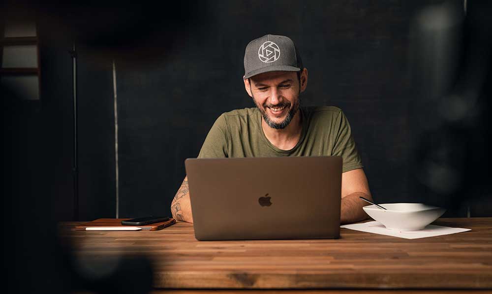 Mann mit Mütze arbeitet am Laptop, sitzt am Holztisch, Kurs-Thumbnail