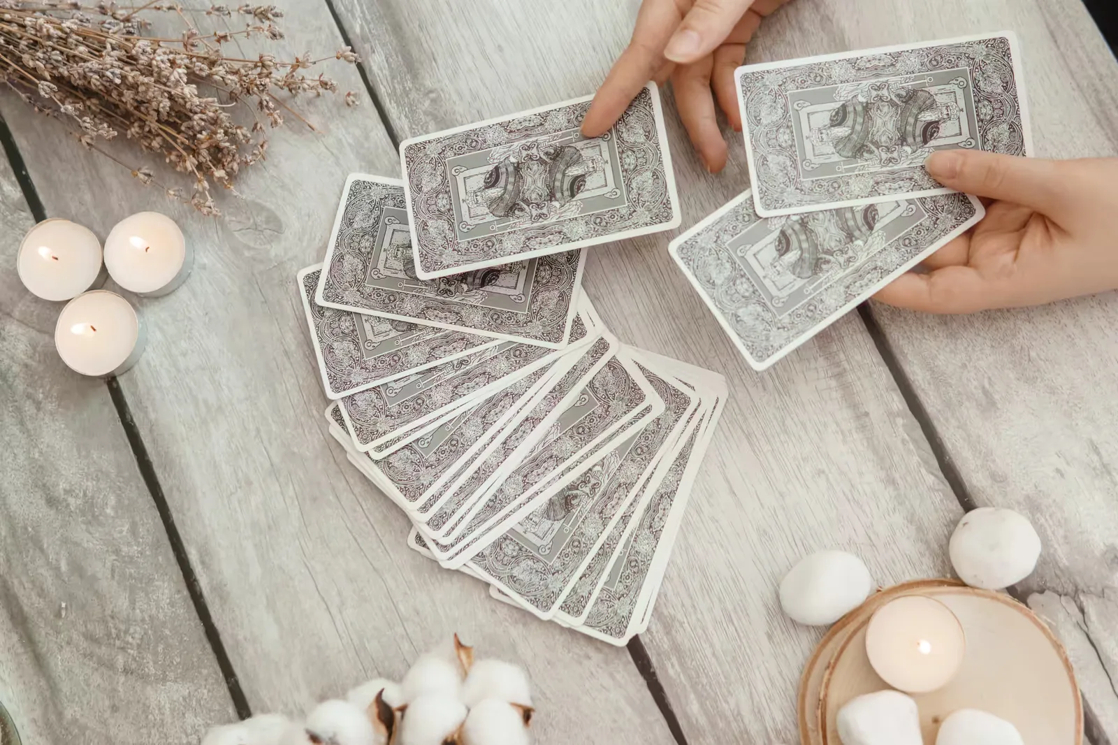 Hände ziehen Tarotkarten, Kerzen und Trockenpflanzen auf Holztisch