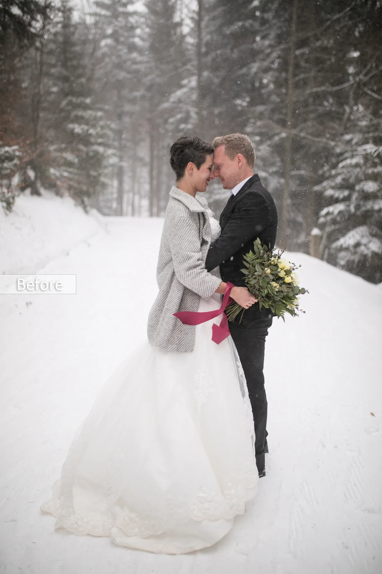 Before-Bild: Brautpaar im Schnee sich umarmend mit farbigem Brautstrauß und winterlicher Waldkulisse