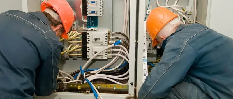 Zwei Elektrofachkräfte in Schutzhelmen bei Arbeit an Elektroanlage mit Schaltkasten