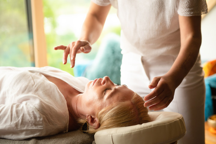 Therapeutin führt Chakra-Energiearbeit an liegender Frau durch in heller Räumlichkeit