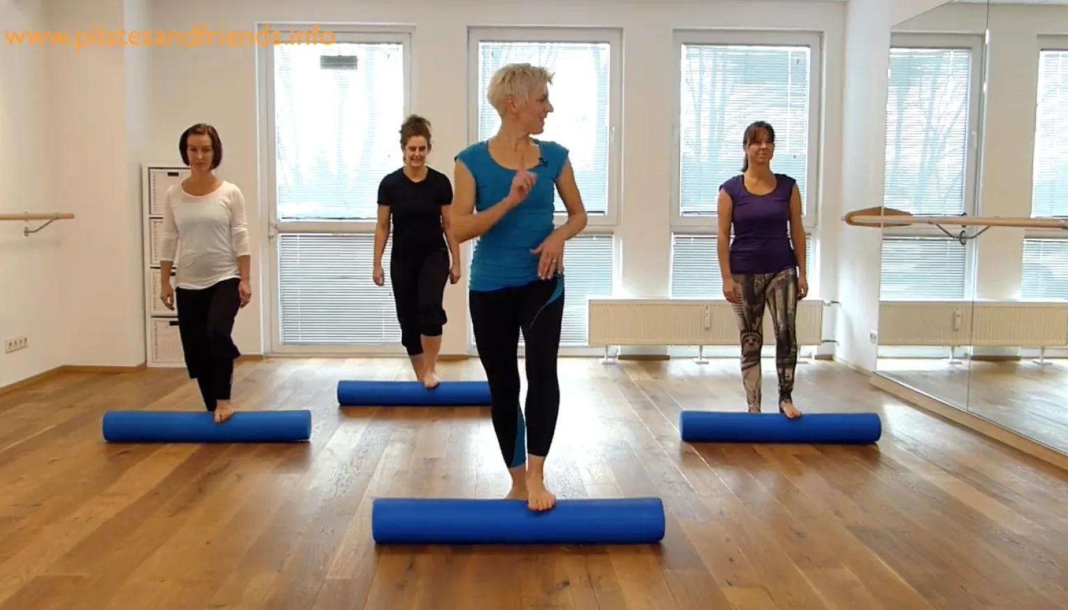 Vier Frauen in Fitness-Kleidung führen ein Lauftraining auf blauen Schaumstoffrollen in einem hellen Tanzstudio durch