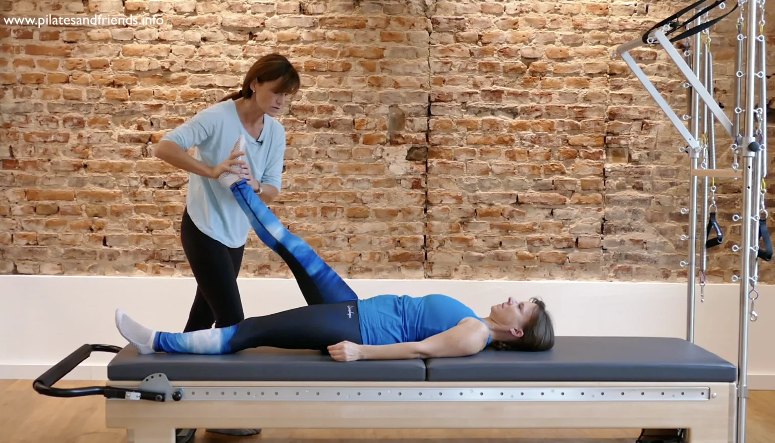 Pilates-Fachkraft nutzt blaues Widerstandsband für Hüfttraining auf Reformer