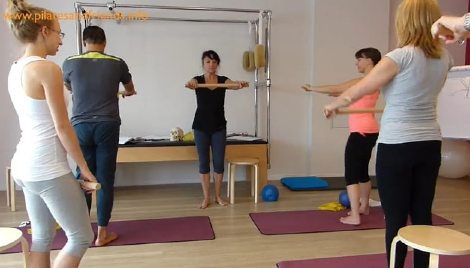 Pilates-Workshop mit Instructor und Teilnehmern, die Trainingsbänder mit ausgestreckten Armen halten
