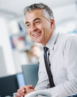 Mann im hellblauen Hemd und Krawatte sitzt lächelnd am Schreibtisch, Profilbild für Testimonial