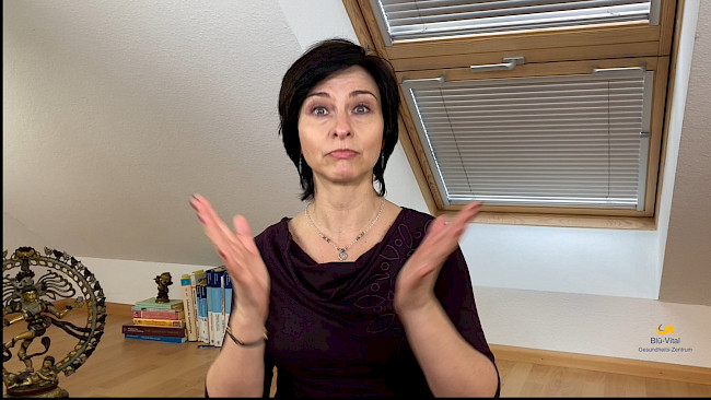 Nicole Blümlinger vor dem Schreibtisch sprechend, braunes Oberteil, Gesten mit erhobenen Händen, Studioumgebung mit Wanddeko